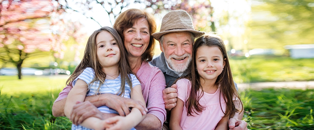 Senior grandparents with granddaughters sitting outside in spring nature, looking at camera.