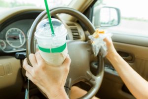 image of woman's hands on steering wheel with coffee and breakfast in her hands distracted driving